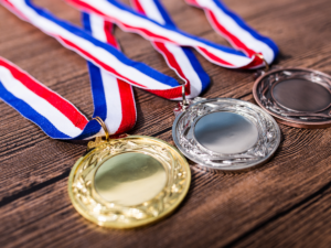 1st, 2nd, 3rd place medals stacked on table with red, white and blue ribbons attached.