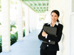 Woman realtor standing with notebook in arms in front of property.