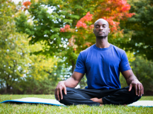 Man sitting in lotus yoga position on mat in park.