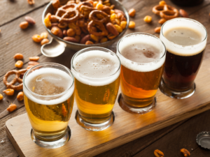 Flight of 4 beers from light to dark with bowl of snacks in background.