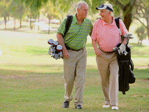 2 gentlemen dressed in khaki pants and polo shirts walking on golf course carrying their golf bags while talking with each other.