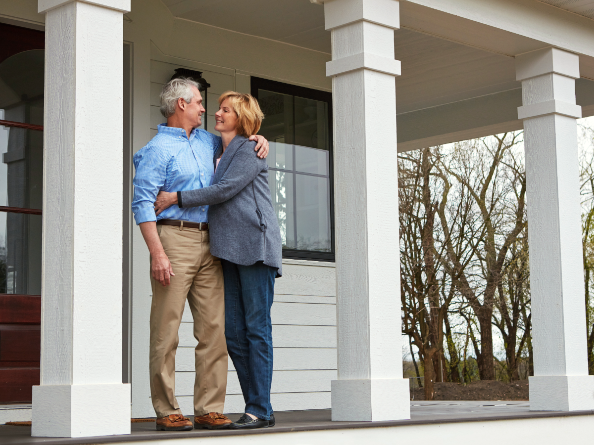 Senior couple with arms around each other standing on front porch of their home for article Retiring in Houston: 9 Outstanding Places to Live for newcomers moving to Houston.