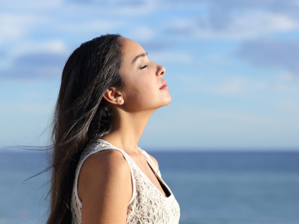 Profile of woman with long straight brown hair with eyes closed and chin up in front of large body of water in background for article 10 Top Resources: women's healthcare in Houston for newcomers moving to Houston.