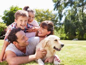 Family of mom, dad, son, and daughter piled up with dog outdoors on the grass smiling and laughing for article Moving to Houston with a Family for newcomers moving to Houston.