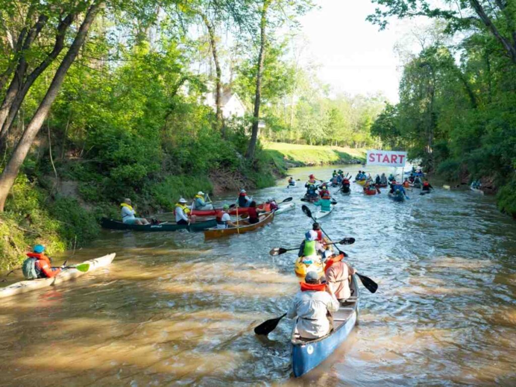 Image of kayakers going down river under start sign for Buffalo Bayou Regatta for article March Events in Houston for newcomers moving to Houston.