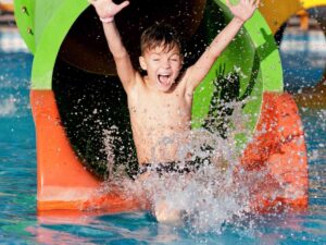 Boy coming out of the end of waterslide tube with hands in air for article Waterparks in the Houston Area: 10 Amazing Parks Newcomers Must Visit for newcomers moving to Houston.