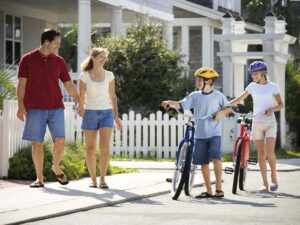 Mom and dad walking on sidewalk in front of house with 2 kids walking their bikes beside them for article Best Neighborhoods in Houston for Families