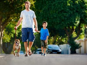 Father and son in cargo shorts and tshirts walking dog in family friendly neighborhood for article Living in The Woodlands vs Katy: Which is Right for You?